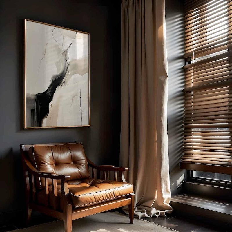Brown leather armchair in a dark, moody office with oversized abstracrt wall art with black, beige and white colors and a black frame.