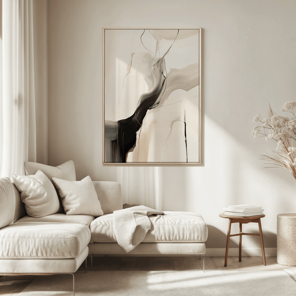 Black and beige abstract wall art in a light wood frame above a cream sofa in a bright, minimal living room