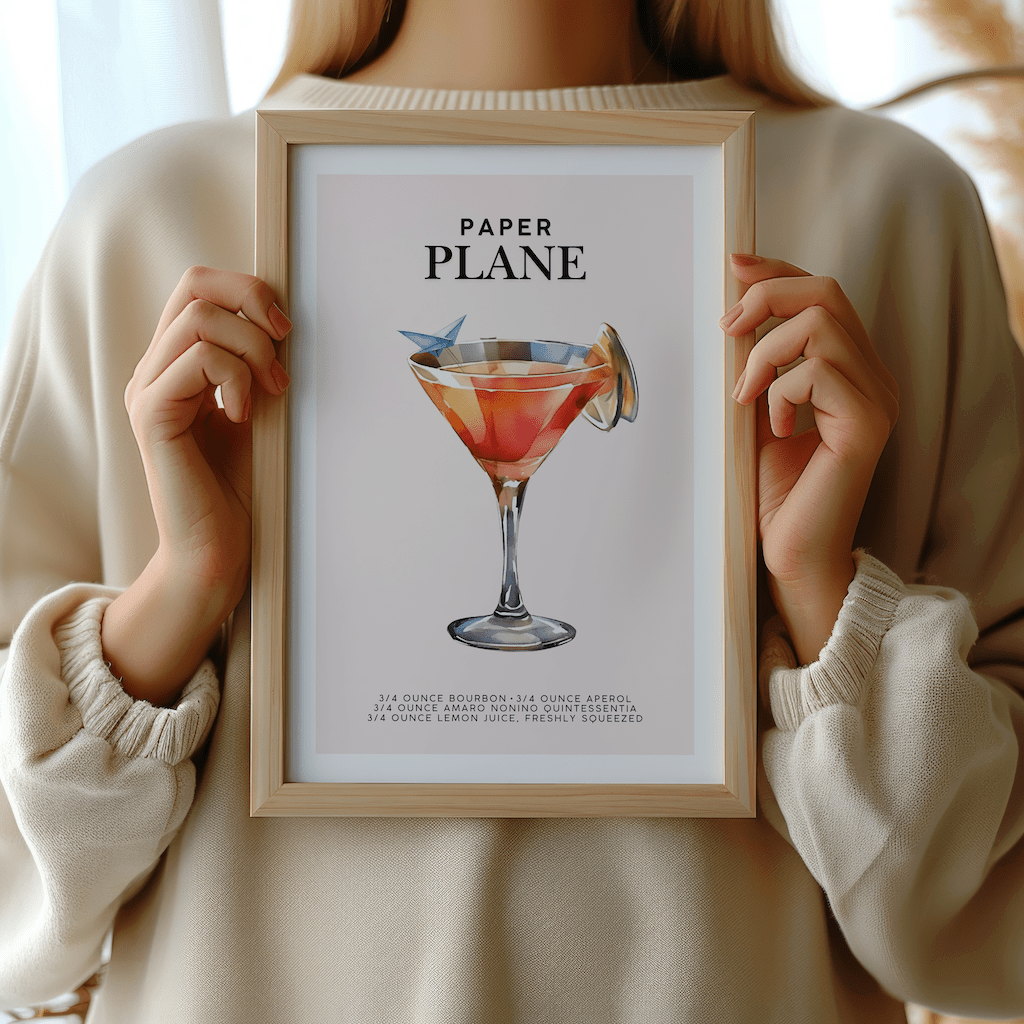 Woman in a cream sweater holding a framed Paper Plane cocktail print