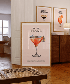 Paper Plane print in a bar cart gallery wall beside espresso martini and Aperol spritz prints on a wooden sideboard
