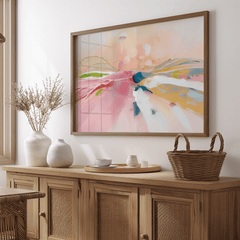 Pastel abstract landscape print in a natural wood frame above a wooden sideboard with dried flowers and a woven basket