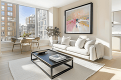 Pastel abstract landscape art in a black frame above a white sofa and black coffee table in a bright modern city apartment