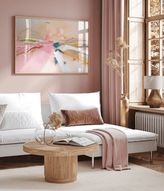 Pastel abstract landscape print in a natural wood frame on a blush pink wall above a white chaise sofa with pampas grass and a round wood coffee table