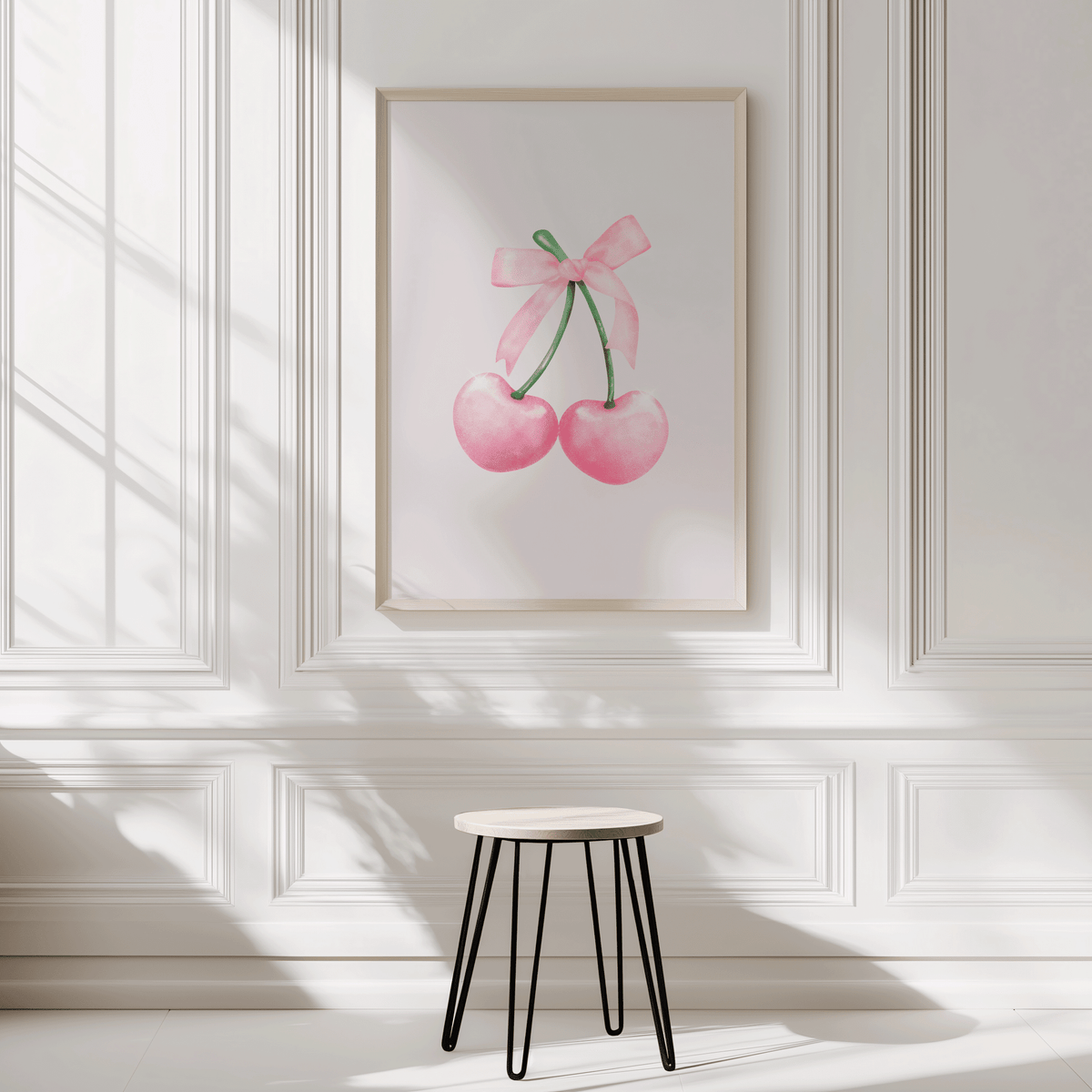 Framed artwork of pink cherries with a coquette bow on a white wall with wainscoting.
