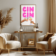 Pink cin cin print in a natural frame above a gold bar cart between two cream armchairs