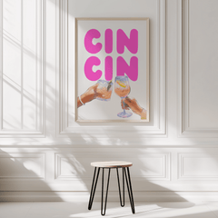 Pink cocktail print in a natural frame on a white panelled wall above a black stool