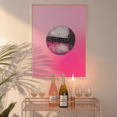 Pink disco ball print in a natural frame above a glass bar cart with wine bottles and a candle