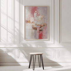 Modern pink and gold abstract art design trending among minimalist canvas wall art buyers. Artwork has a light wooden frame and is on a white panelled wall with a wooden stool in front.