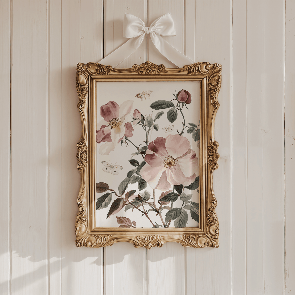 Pink rose and butterfly nursery print in an ornate gold frame with a white bow on a white panelled wall