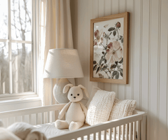 Pink rose nursery print above a white crib with a teddy bear by a sunny window