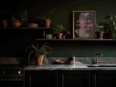 Queen of Canceling Plans print on a dark green shelf with plants and pottery