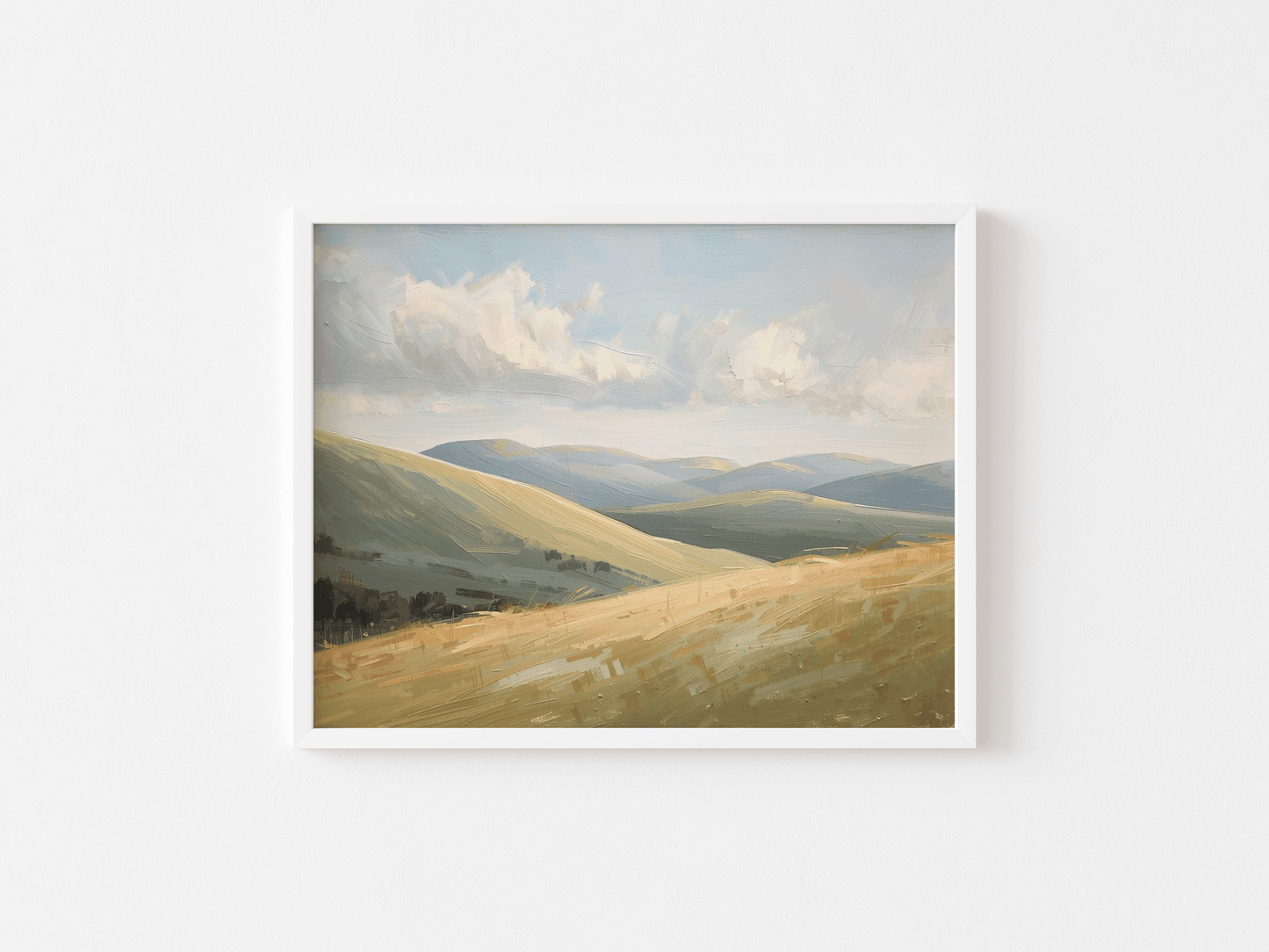 A white-framed landscape wall art print of rolling green and beige hills under a cloudy blue sky.