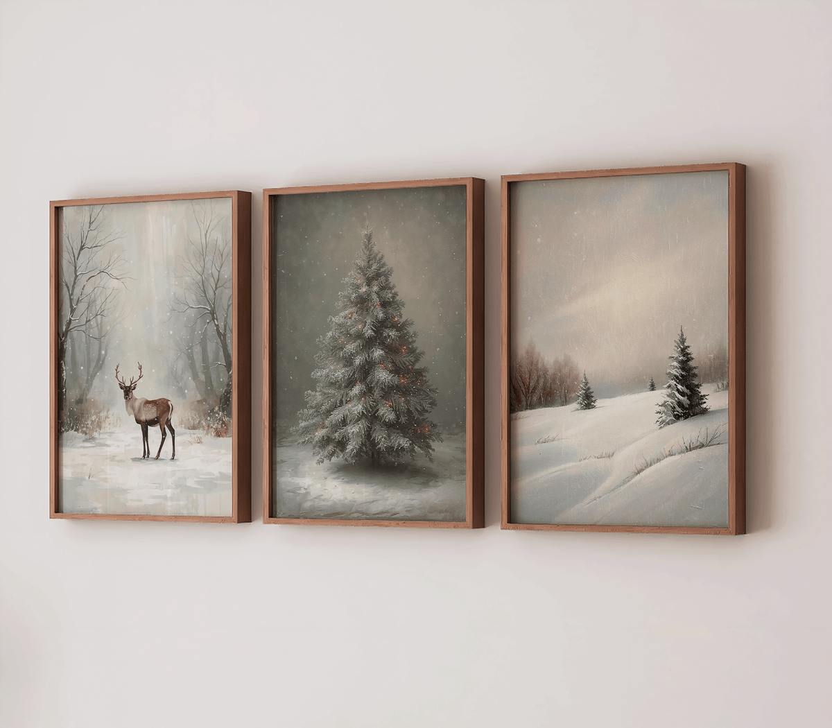 Three vertical wood-framed winter prints hung side by side on a white wall, featuring a deer in the snow, a lit Christmas tree, and a snowy hill with evergreen trees