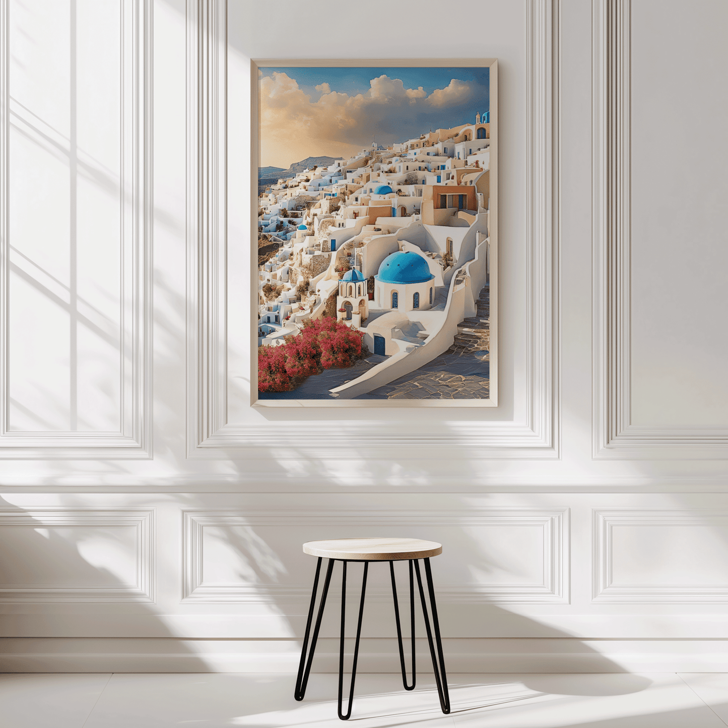 Framed artwork of a Greek village scene in Santorini Greece on a white wall with a stool in front. 