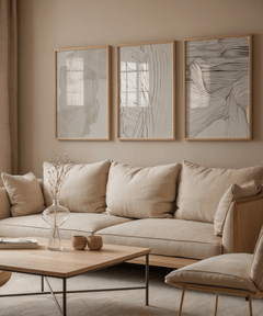 Set of 3 triptych framed canvas wall art prints above a beige sofa in a minimalist living room with wood accents and boho dried flowers