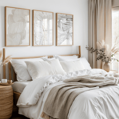 Set of 3 abstract, neutral and minimal framed wall art prints above a bed with a wooden bed frame in a boho bedroom. Artwork is a mix of black and white lines, white on white faux paint texture, and beige and white smooth, rounded line design illustration.