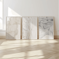 Three framed abstract wall art prints in black, white, beige tones with faux texture on a light wooden floor.