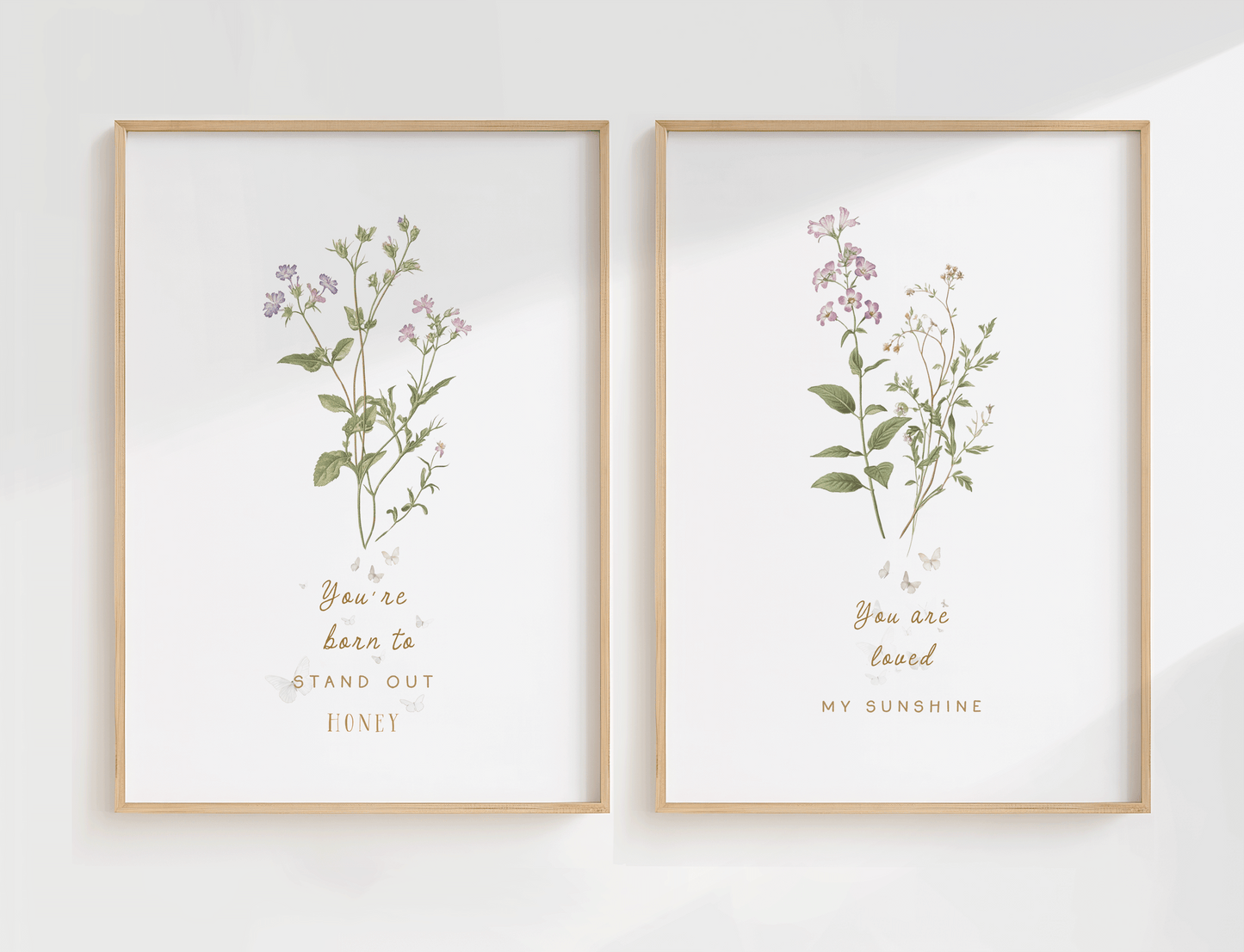 Set of two botanical nursery wall art prints featuring soft florals and greenery in matching wooden frames, styled side by side on a light wall.