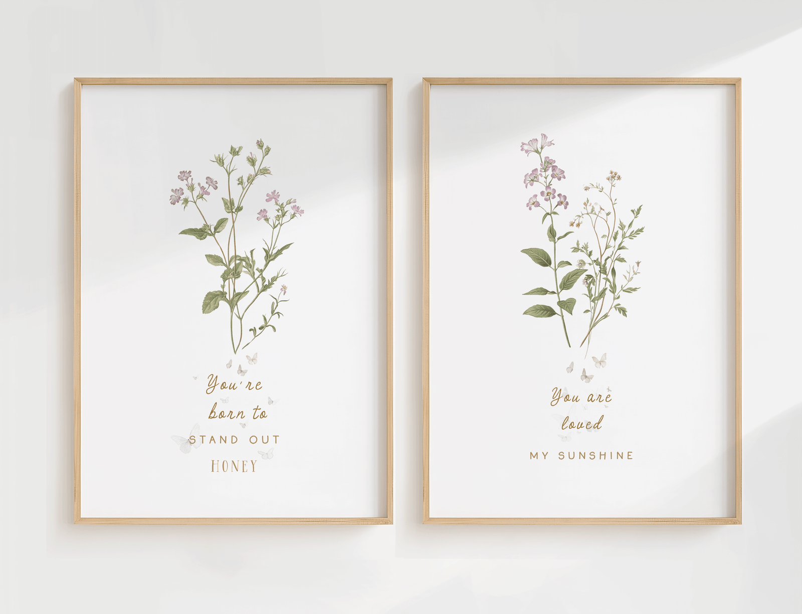 Set of two botanical nursery wall art prints featuring soft florals and greenery in matching wooden frames, styled side by side on a light wall.