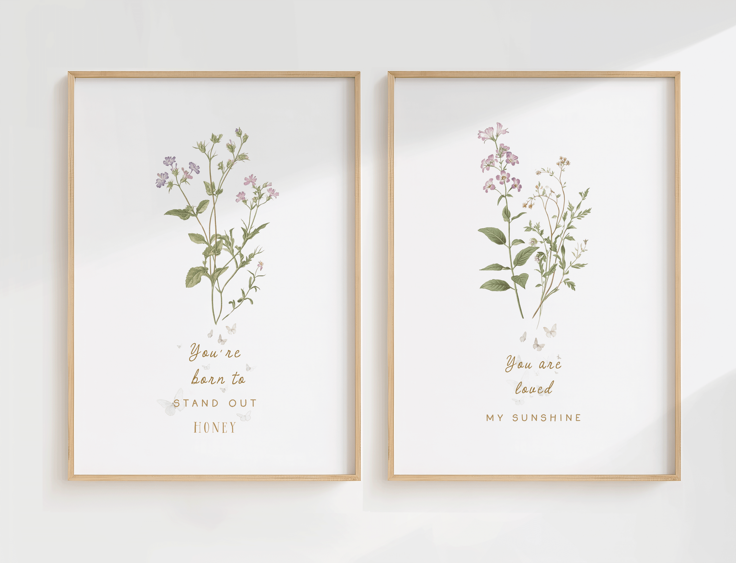 Set of two botanical nursery wall art prints featuring soft florals and greenery in matching wooden frames, styled side by side on a light wall.