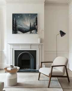 Framed starry winter night Christmas wall art with snowy mountain scene and glowing stars, displayed above a white fireplace in a neutral modern living room with soft natural light.
