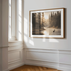Deer by the lake forest wall art in a gold frame, styled in a bright sunlit corner with white paneled walls.