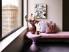 Toasting hands wall art above a pink upholstered bench with patterned pillows beside a city window