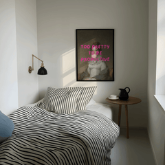 Modern bedroom with striped bedding, side table, and framed modern funny wall art print with 'too pretty to be productive' text.