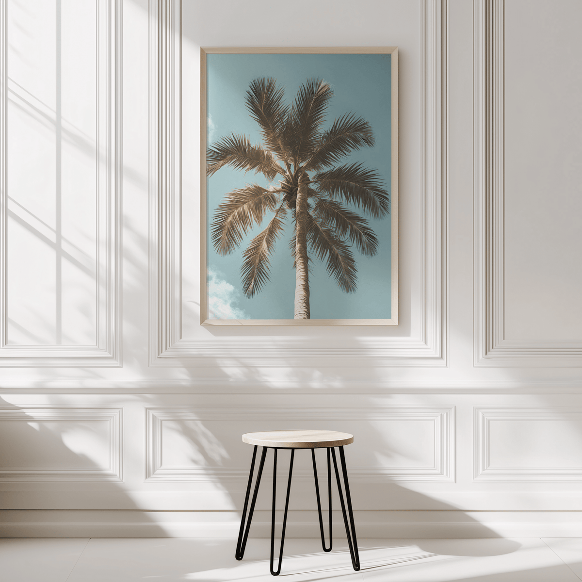 Tropical palm tree wall art framed on modern white panelled wall in neutral interior with a small stool
