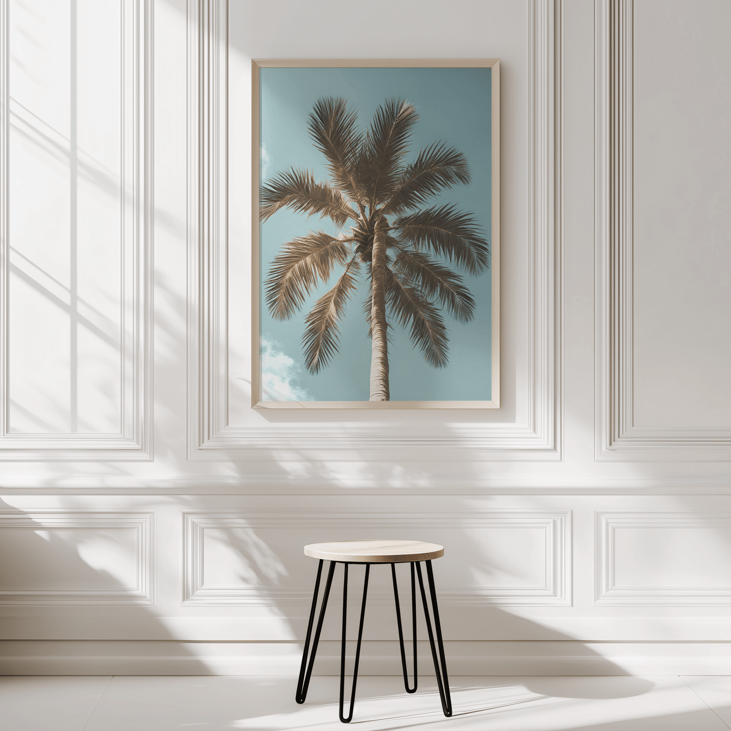 Tropical palm tree wall art framed on modern white panelled wall in neutral interior with a small stool