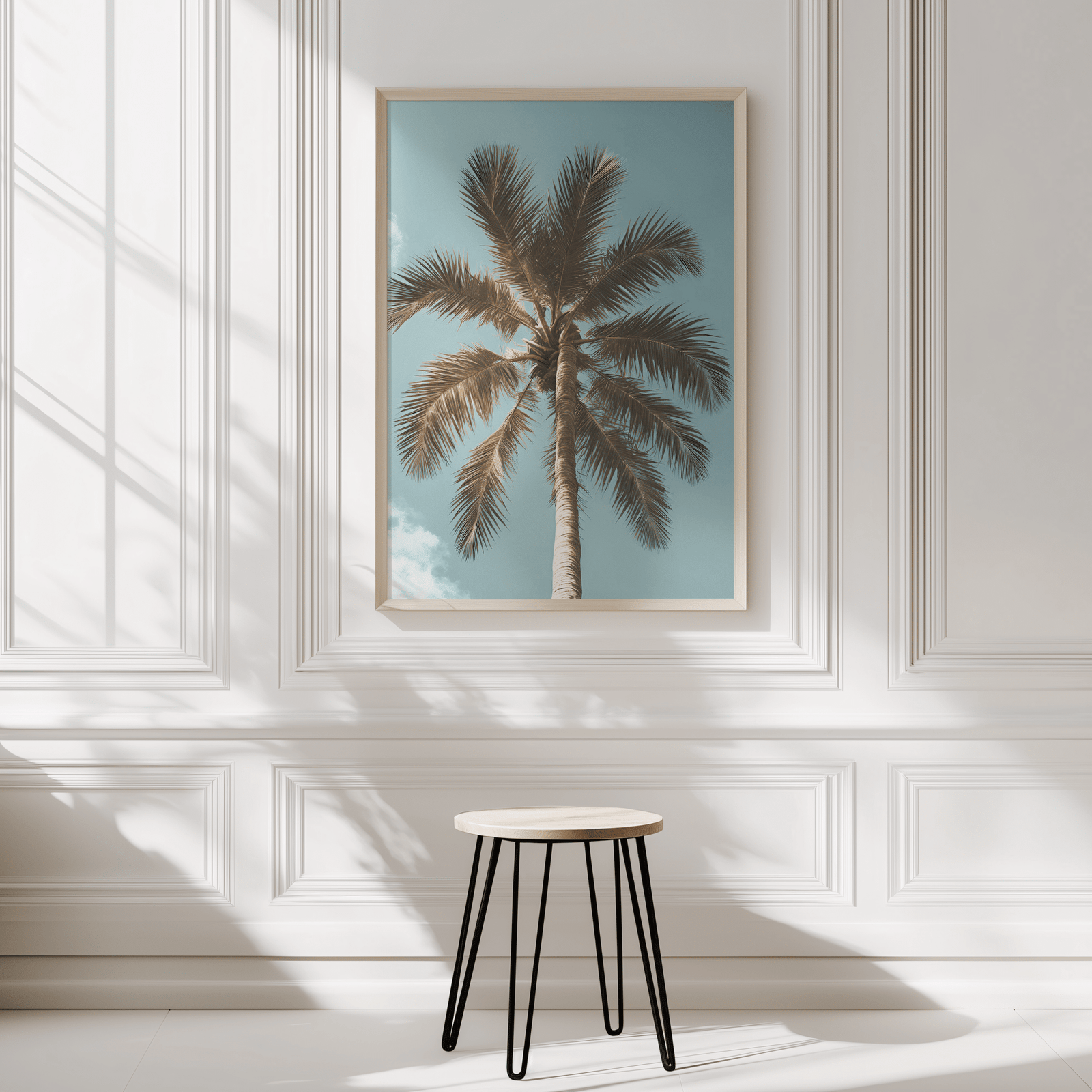 Tropical palm tree wall art framed on modern white panelled wall in neutral interior with a small stool