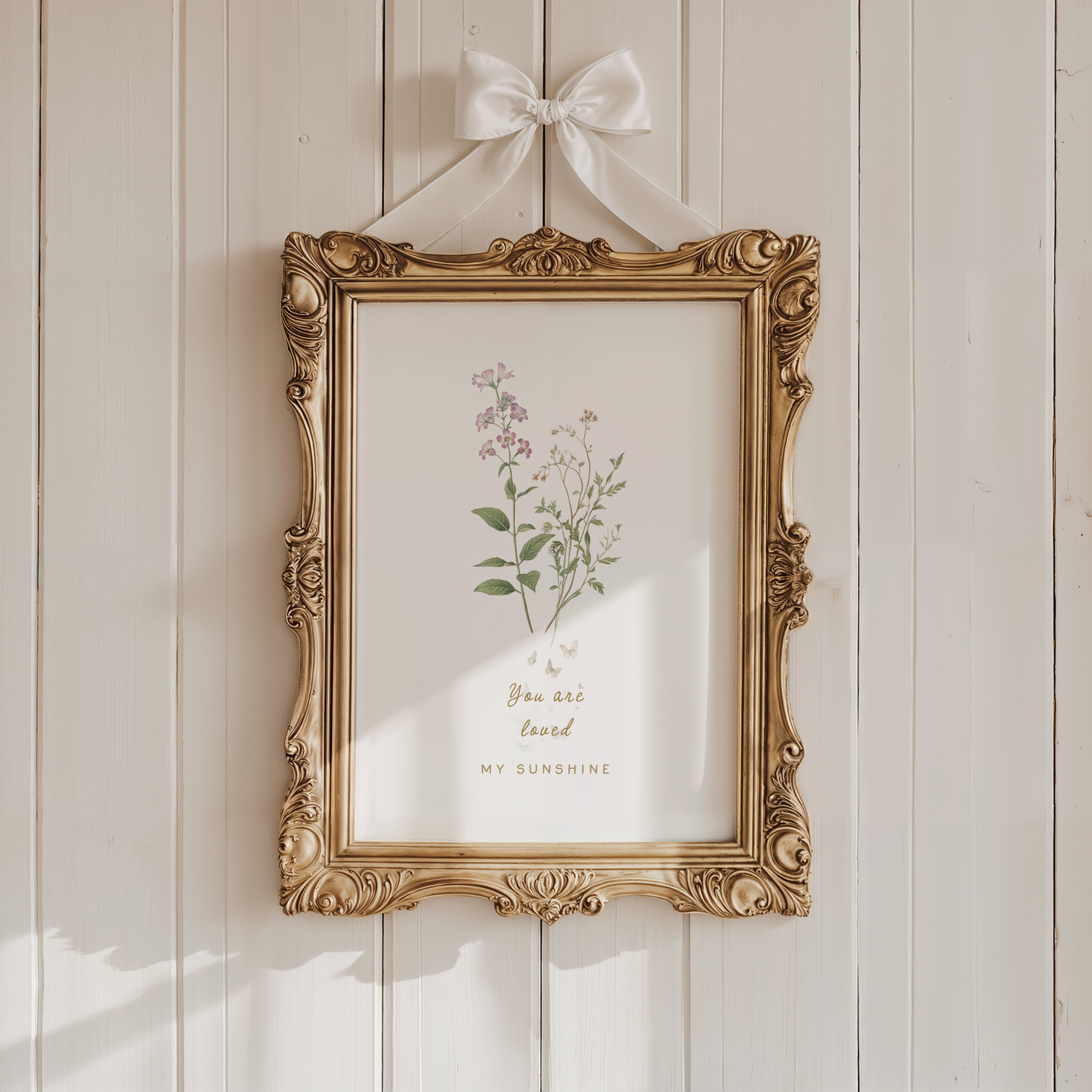 Vintage-style nursery wall art with soft florals displayed in an ornate gold frame against a warm neutral wall.