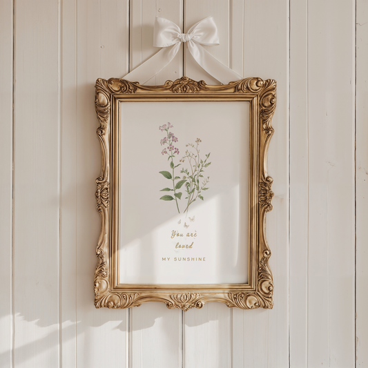 Vintage-style nursery wall art with soft florals displayed in an ornate gold frame against a warm neutral wall.