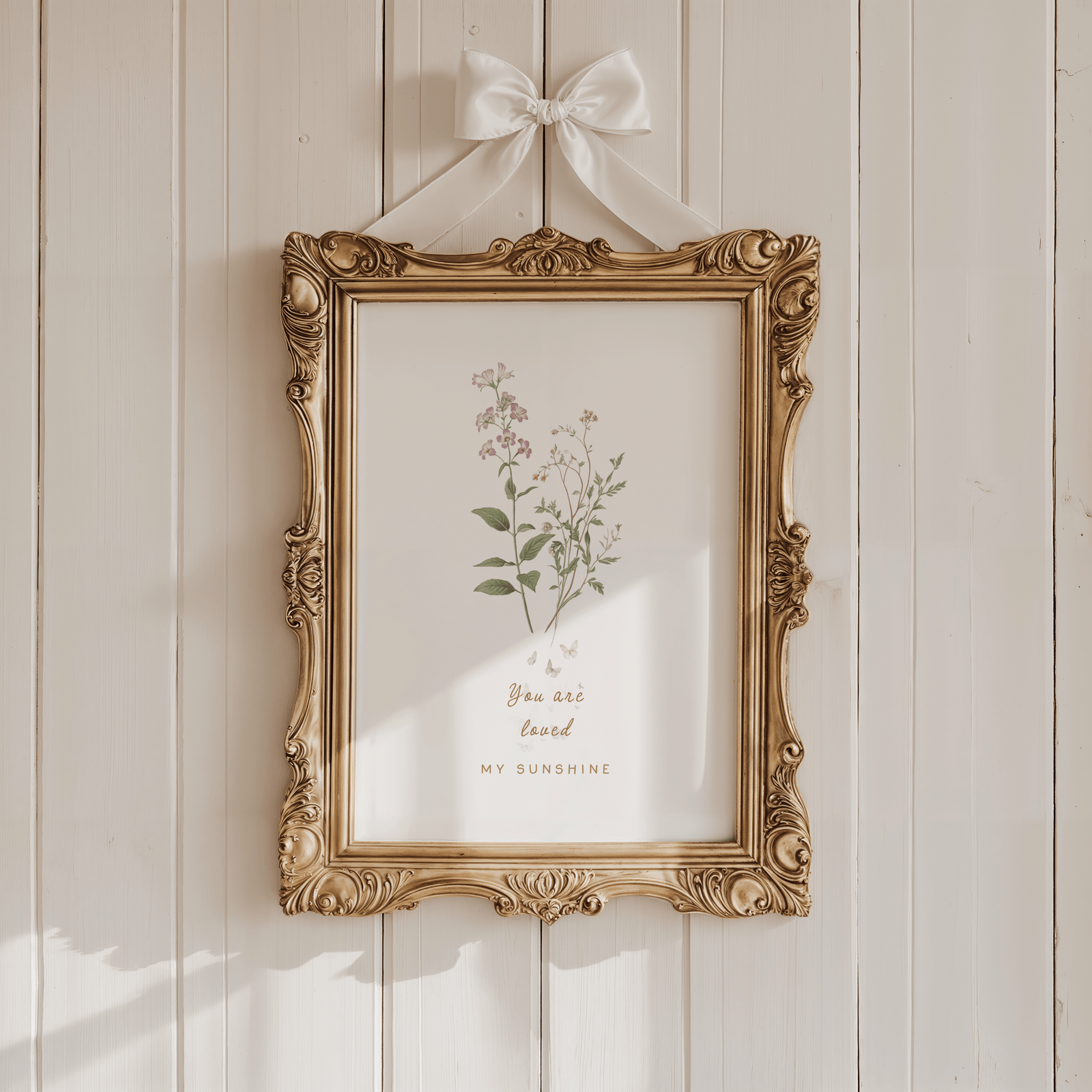 Vintage-style nursery wall art with soft florals displayed in an ornate gold frame against a warm neutral wall.