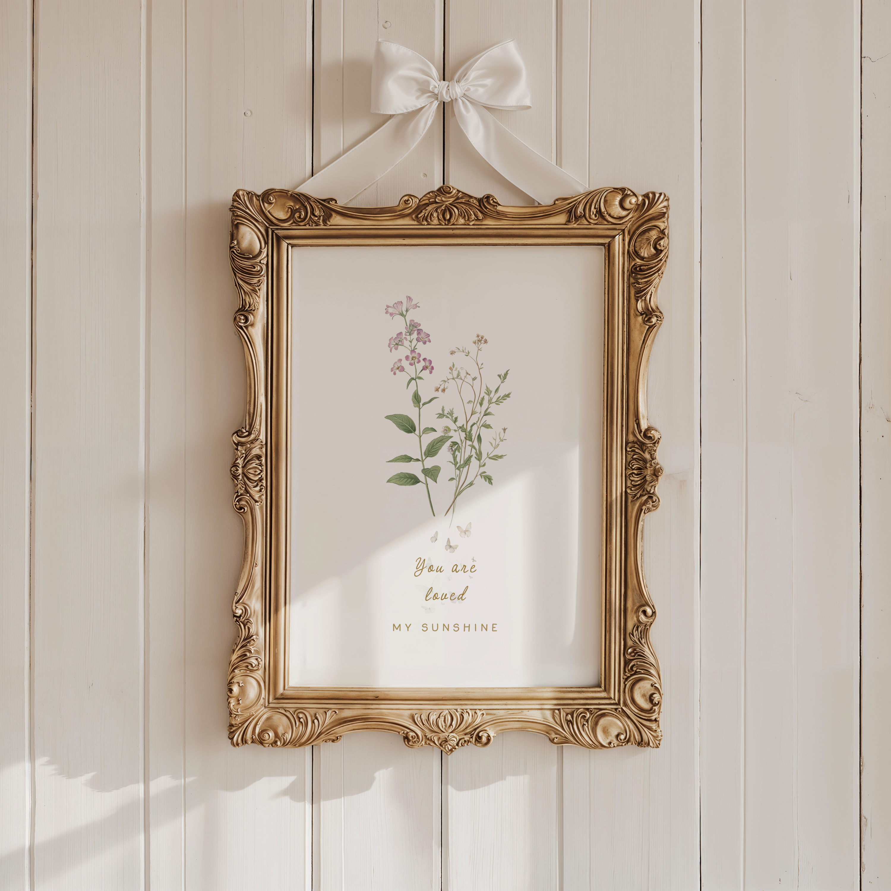 Vintage-style nursery wall art with soft florals displayed in an ornate gold frame against a warm neutral wall.