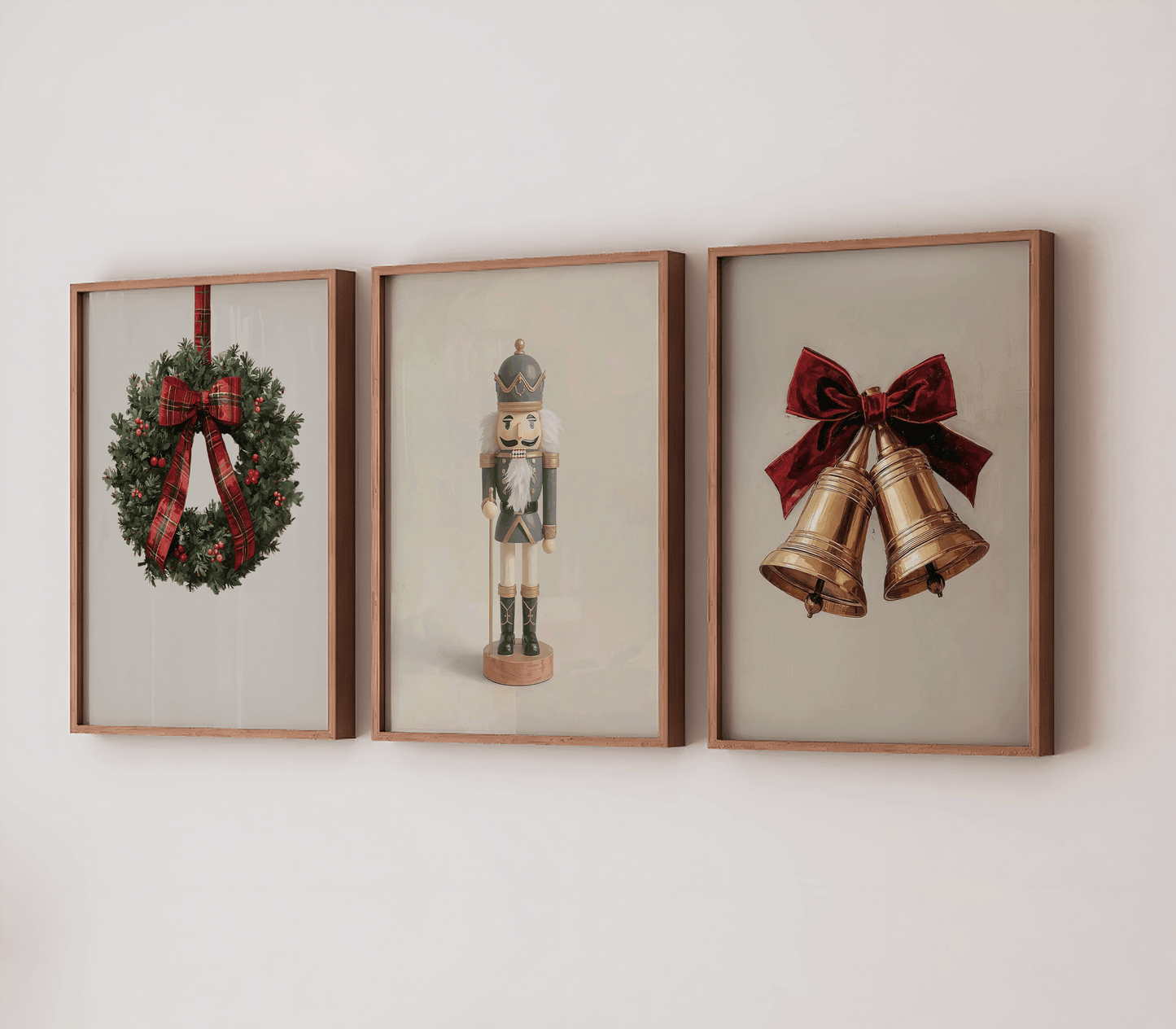 Three framed Christmas prints on a neutral wall featuring a plaid ribbon wreath, a vintage navy-and-gold nutcracker, and a pair of gold bells tied with a deep red velvet bow
