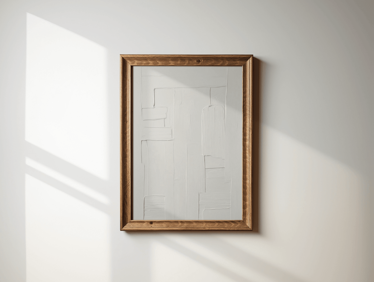 Wooden-framed all-white faux-textured minimal abstract wall art print on a white wall with sunlight casting shadows.