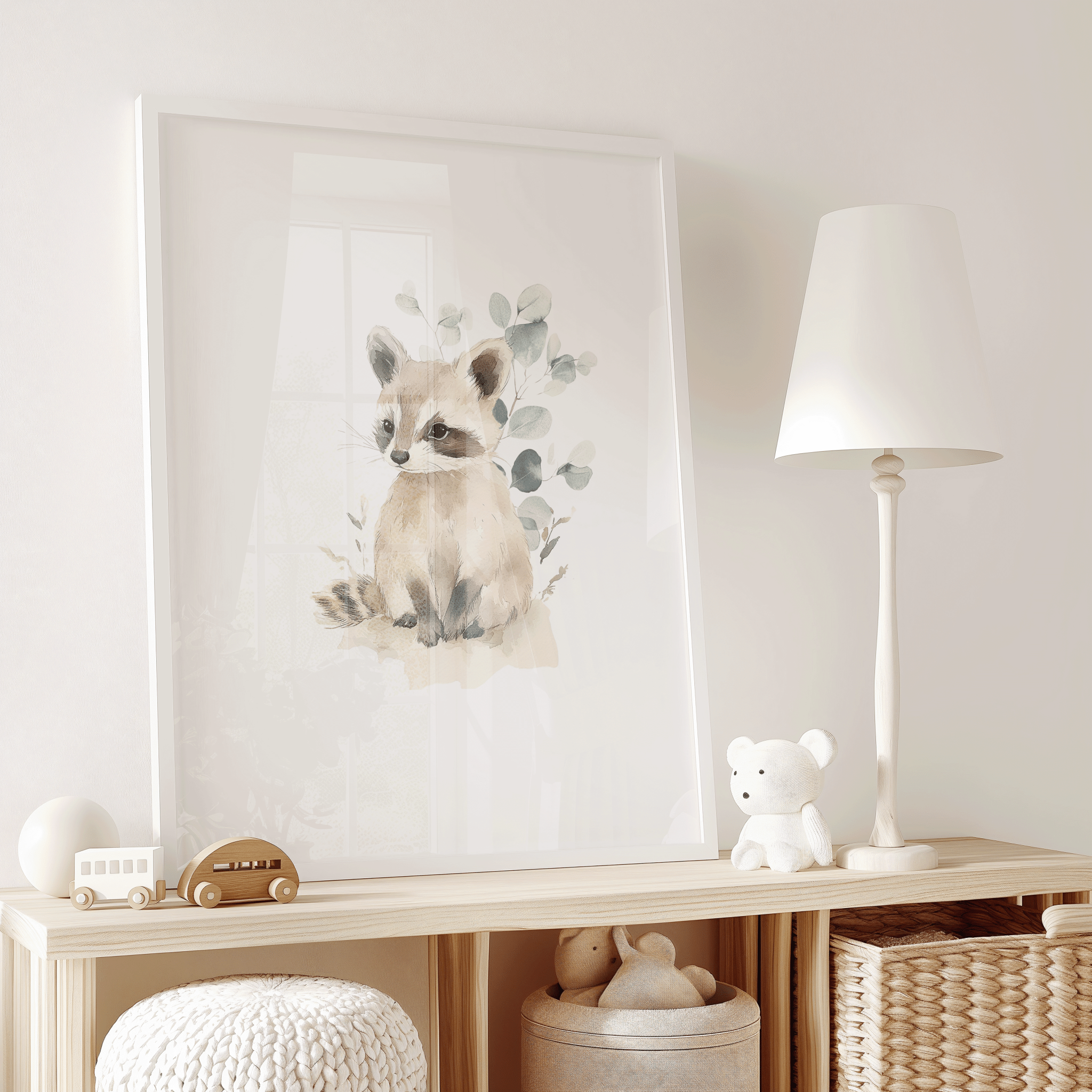 Neutral minimal woodland nursery animal art of a baby raccoon in a watercolor style with soft browns, beiges, and greens with eucalyptus leaves in a white frame on a wooden shelf in a kid's play room.