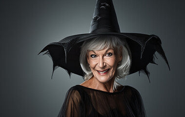 A good old smiling witch in a black dress and a magic hat on a dark background